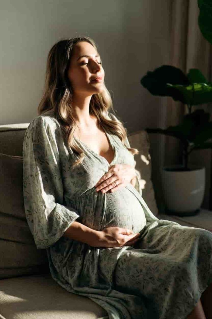 Donna in gravidanza seduta sul divano con le mani sul pancione — perdite in gravidanza